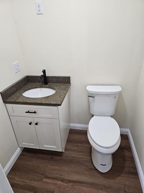 half bathroom featuring baseboards, vanity, toilet, and wood finished floors