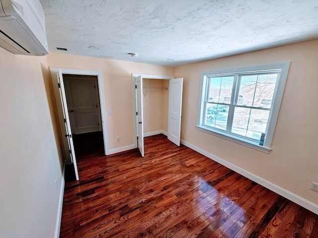 unfurnished bedroom with dark wood finished floors, a closet, a wall mounted AC, a textured ceiling, and baseboards