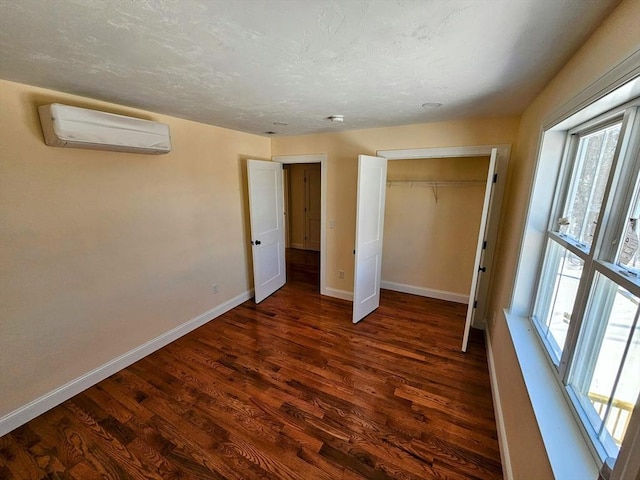 unfurnished bedroom featuring dark wood finished floors, a closet, a wall mounted AC, a textured ceiling, and baseboards