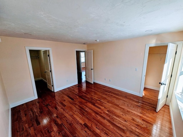 unfurnished bedroom featuring wood-type flooring, baseboards, and a walk in closet