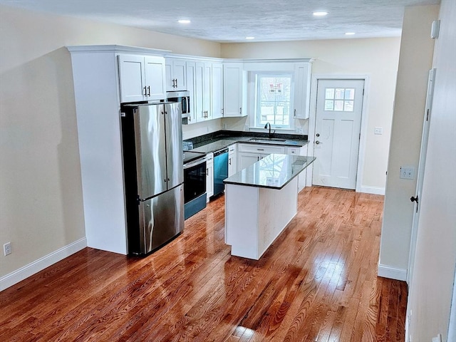 kitchen with stainless steel appliances, a sink, white cabinets, hardwood / wood-style floors, and dark countertops