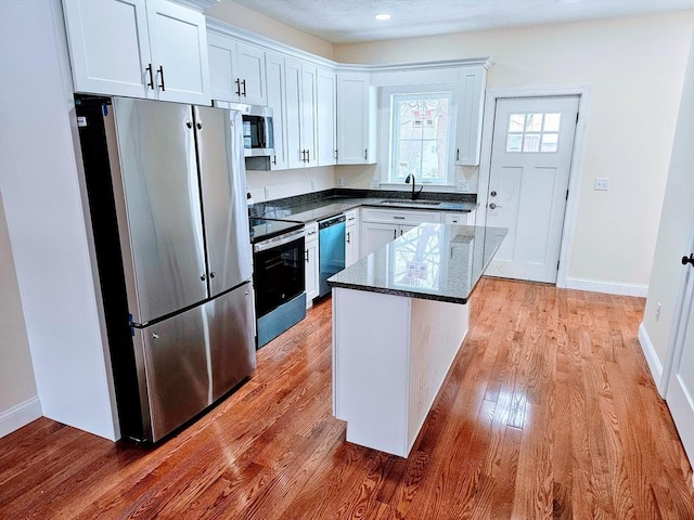 kitchen featuring stainless steel appliances, a kitchen island, a sink, white cabinets, and light wood-style floors