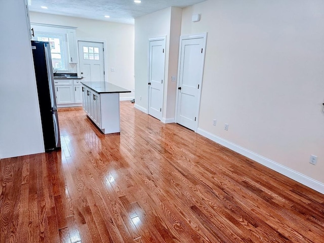 kitchen featuring baseboards, light wood finished floors, freestanding refrigerator, and white cabinets