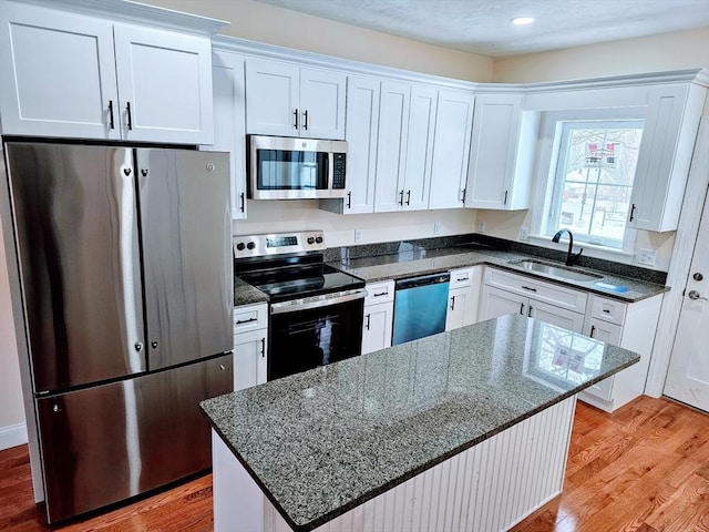 kitchen featuring stainless steel appliances, white cabinets, a sink, dark stone counters, and light wood-type flooring