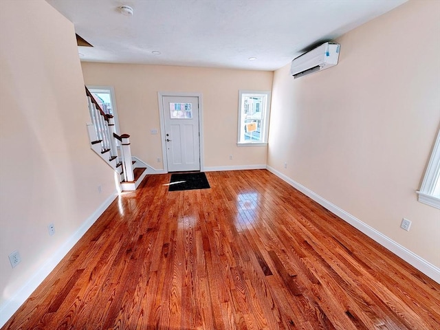 foyer featuring an AC wall unit, wood-type flooring, stairway, and baseboards