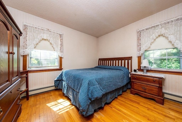 bedroom with a baseboard heating unit, light wood-type flooring, a textured ceiling, and multiple windows