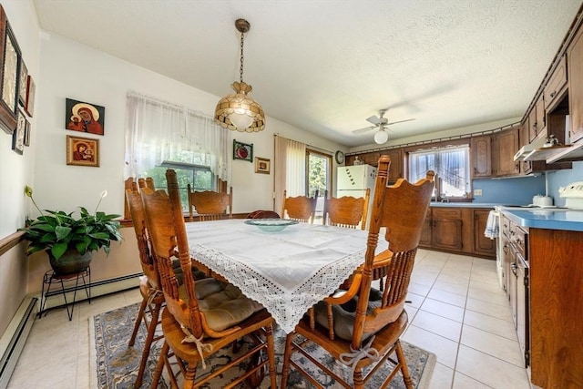 tiled dining room with a textured ceiling, a wealth of natural light, a baseboard heating unit, and ceiling fan