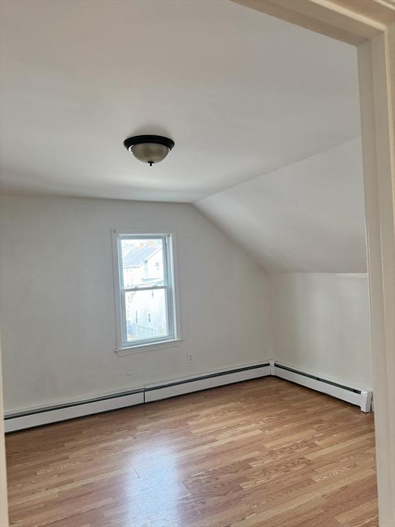 additional living space featuring vaulted ceiling, a baseboard radiator, and light hardwood / wood-style flooring