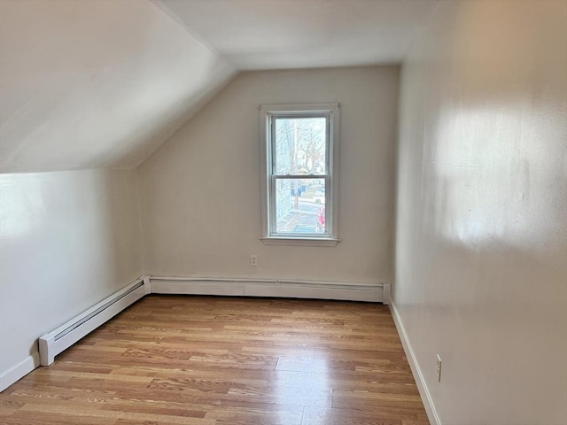 additional living space with a baseboard heating unit, light hardwood / wood-style flooring, and vaulted ceiling