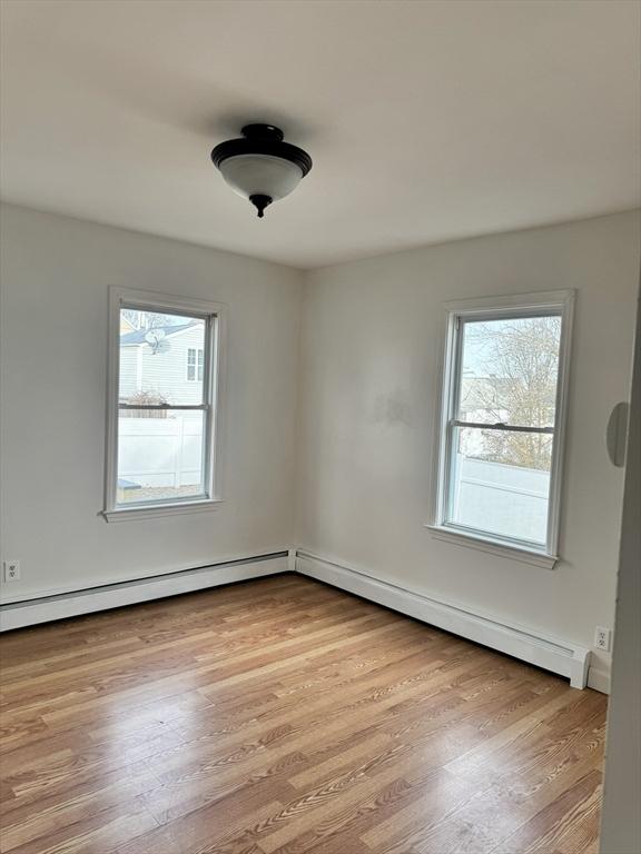 spare room with a baseboard heating unit, a healthy amount of sunlight, and light hardwood / wood-style floors