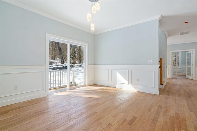 spare room with light wood finished floors, visible vents, crown molding, and a wainscoted wall