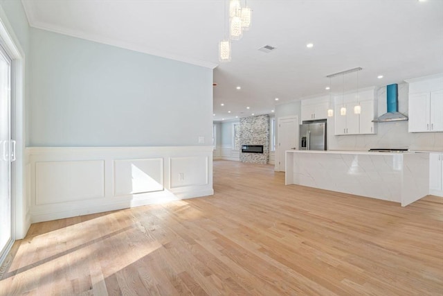 interior space with light wood finished floors, stainless steel fridge with ice dispenser, open floor plan, white cabinetry, and wall chimney exhaust hood