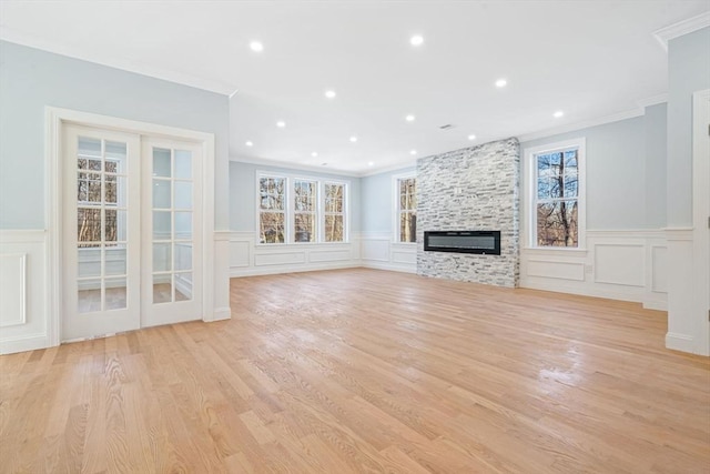 unfurnished living room with a large fireplace, plenty of natural light, crown molding, and light wood-style floors