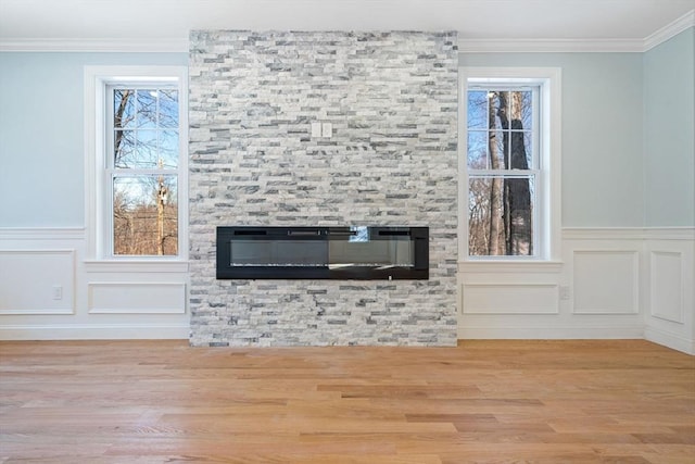 unfurnished living room with plenty of natural light, a fireplace, ornamental molding, and wood finished floors