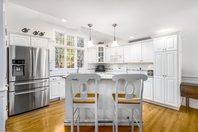 kitchen featuring white appliances, white cabinets, a center island, and hanging light fixtures