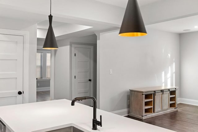 kitchen featuring dark wood-style flooring, hanging light fixtures, light countertops, baseboards, and a sink