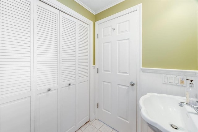 bathroom featuring wainscoting, a sink, tile patterned floors, ornamental molding, and a closet