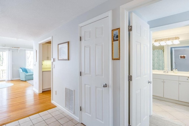 hallway with a sink, baseboards, light tile patterned flooring, and visible vents