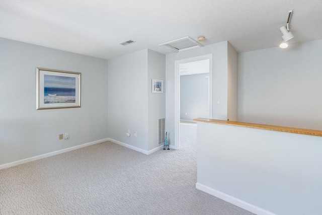 empty room featuring attic access, visible vents, light colored carpet, track lighting, and baseboards