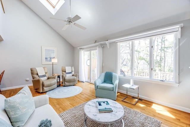 living area with a skylight, baseboards, ceiling fan, and wood finished floors