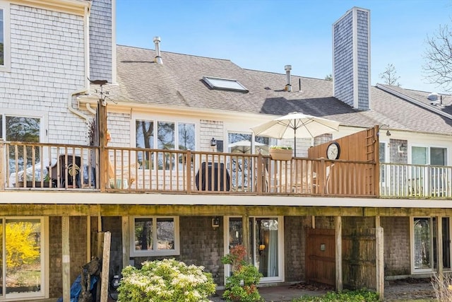 back of house featuring a shingled roof, a chimney, and a deck