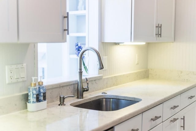 kitchen with a sink, white cabinets, and light stone countertops