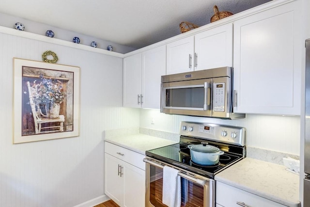 kitchen featuring light stone counters, appliances with stainless steel finishes, wood finished floors, and white cabinets