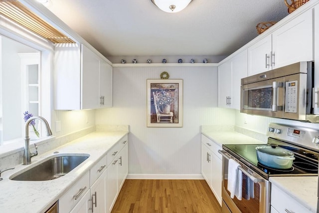 kitchen featuring baseboards, light wood-style floors, white cabinetry, a sink, and appliances with stainless steel finishes