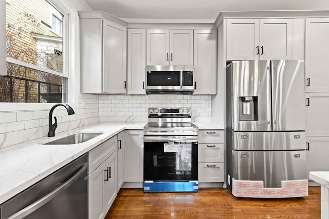 kitchen featuring appliances with stainless steel finishes, dark hardwood / wood-style flooring, tasteful backsplash, light stone counters, and sink