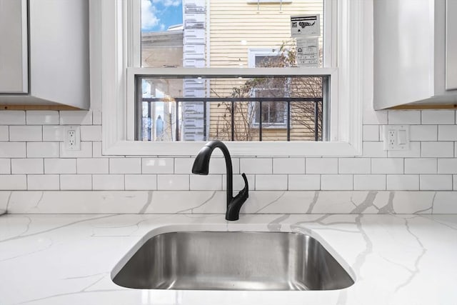 interior details with white cabinets, backsplash, light stone counters, and sink