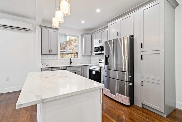 kitchen featuring gray cabinetry, stainless steel appliances, a wall mounted AC, pendant lighting, and a kitchen island