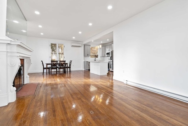 unfurnished living room featuring a wall mounted air conditioner, sink, hardwood / wood-style flooring, and a baseboard heating unit