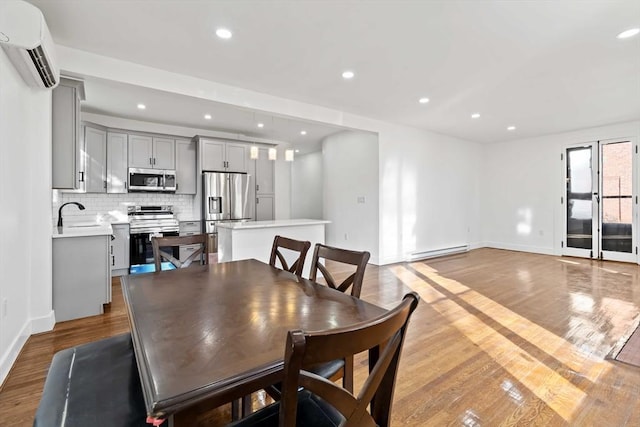 dining area with light wood-type flooring, sink, a wall unit AC, and a baseboard heating unit