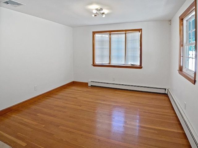 empty room featuring baseboards, baseboard heating, visible vents, and wood finished floors