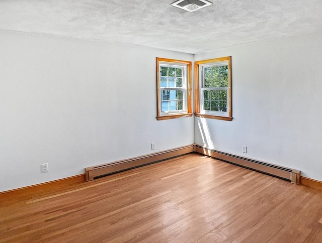 empty room with wood finished floors, a textured ceiling, visible vents, baseboards, and a baseboard radiator