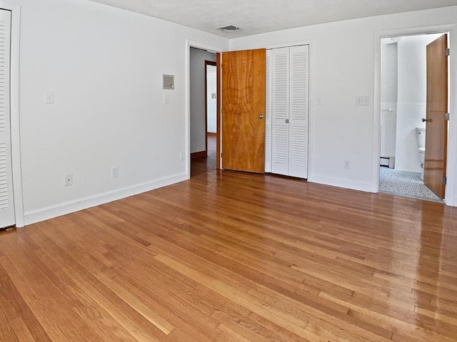 unfurnished bedroom featuring light wood finished floors, visible vents, baseboards, ensuite bath, and a baseboard radiator