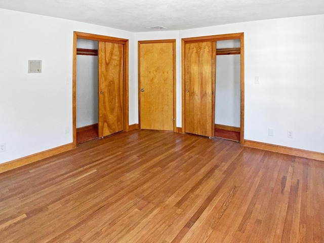 unfurnished bedroom featuring two closets, visible vents, wood finished floors, and baseboards