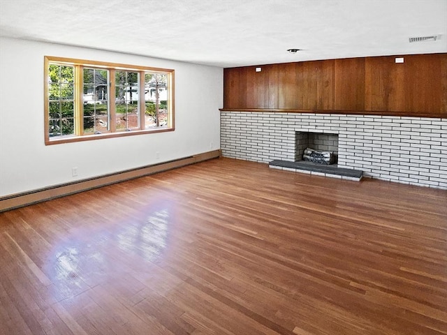unfurnished living room with wood walls, wood finished floors, visible vents, and a baseboard heating unit