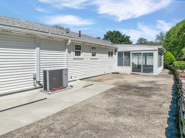 rear view of property with a sunroom, a patio, roof with shingles, and central AC