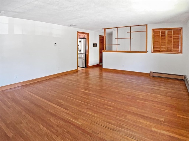 unfurnished room featuring baseboard heating, wood finished floors, and baseboards