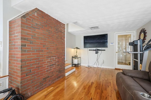 living area with baseboards, brick wall, visible vents, and wood finished floors