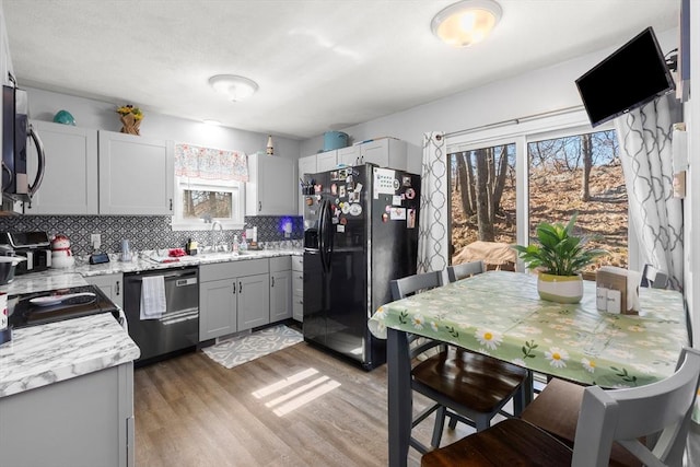 kitchen with light wood finished floors, decorative backsplash, gray cabinets, black appliances, and a sink