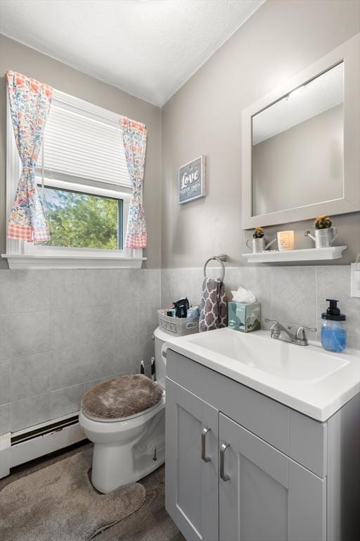 half bath featuring toilet, a baseboard heating unit, tile walls, wainscoting, and vanity