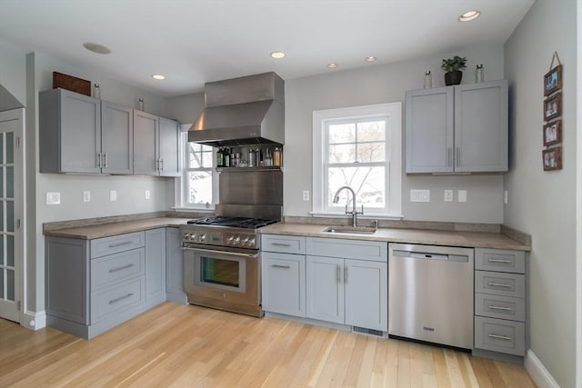 kitchen with a sink, wall chimney range hood, appliances with stainless steel finishes, and a healthy amount of sunlight
