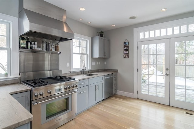 kitchen featuring visible vents, wall chimney exhaust hood, a sink, stainless steel appliances, and light wood-style flooring