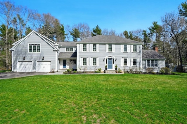 colonial inspired home featuring a chimney, a garage, aphalt driveway, and a front yard