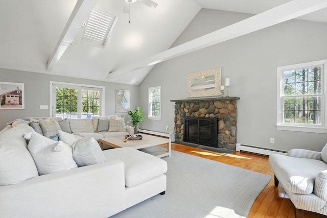 living room featuring a ceiling fan, wood finished floors, a stone fireplace, baseboard heating, and a baseboard radiator
