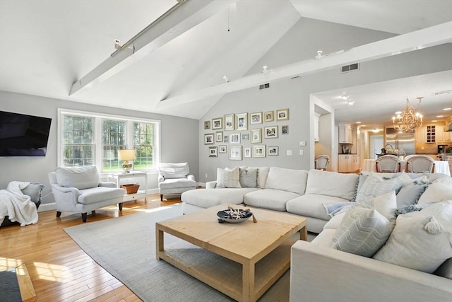 living room with high vaulted ceiling, a notable chandelier, light wood-type flooring, and visible vents