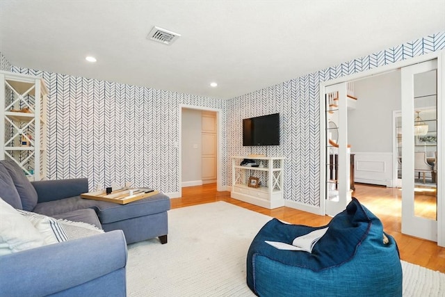 living area with an accent wall, wallpapered walls, wood finished floors, and visible vents