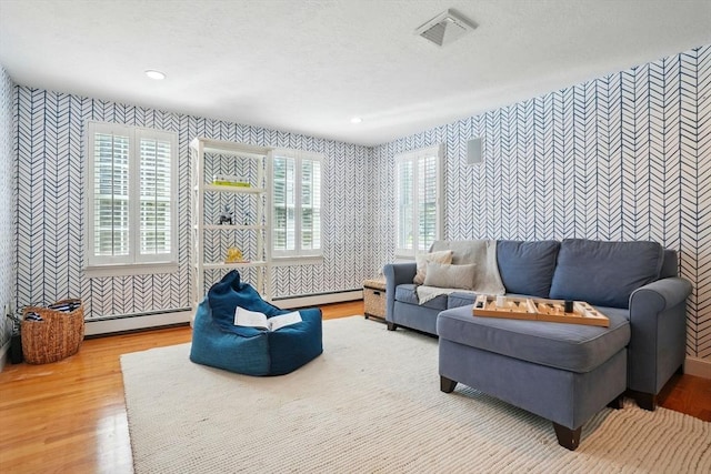 living area featuring baseboard heating, wallpapered walls, wood finished floors, and visible vents